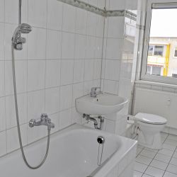 Weiß gefliestes Badezimmer mit Badewanne und großem Fenster